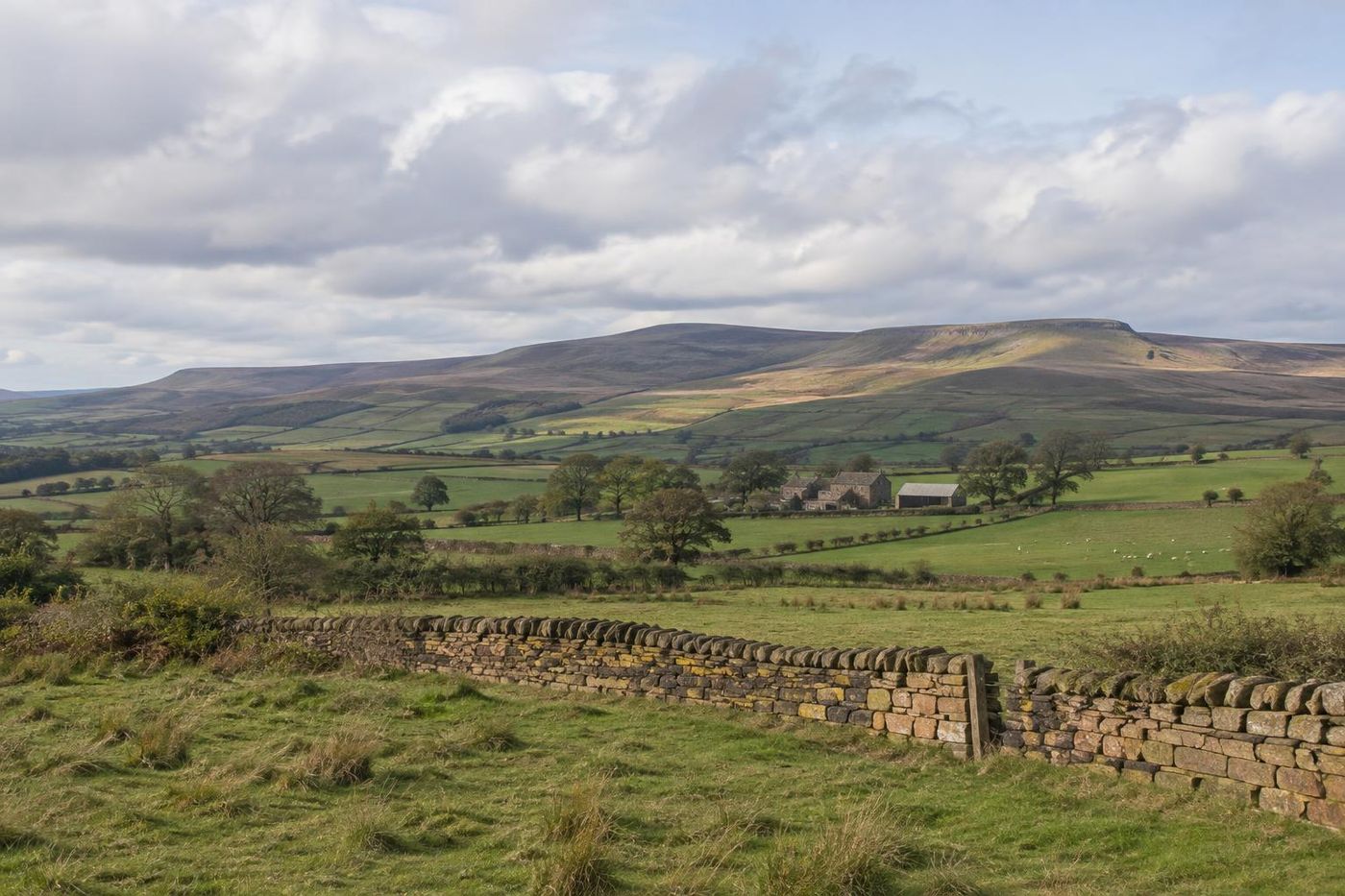 Wide view across Lancashire farmland to distant moorland hills, drystone walls and hedges, broken cloud and moving light.